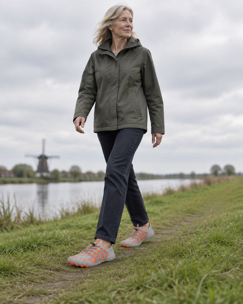 Vrouw van rond de zestig wandelt in de Norvaflex Ridge over een dijkpad langs het water